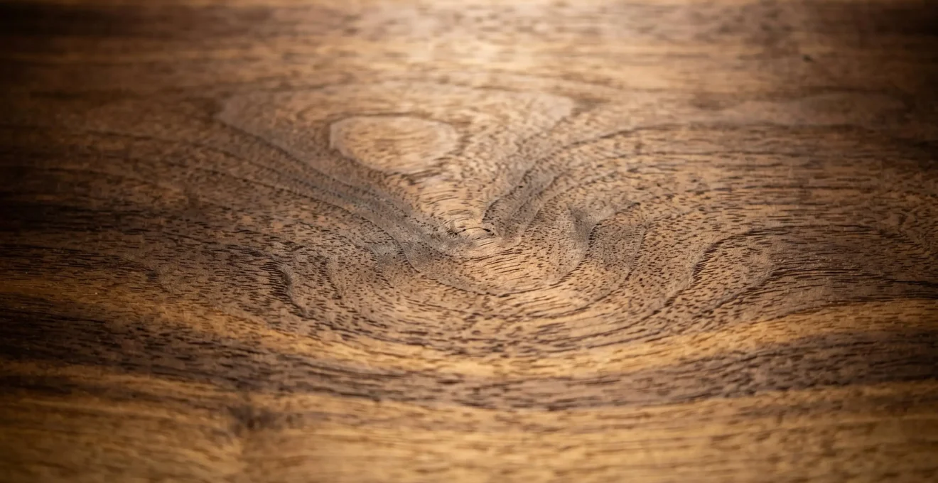Gros plan texture noyer américain huilé révélant veinage naturel et variations chromatiques chocolat à miel sous lumière rasante